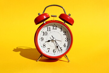 A red alarm clock stands on a yellow background. Time shows half of the ninth.