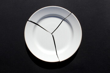 A broken white plate lies on a black background.