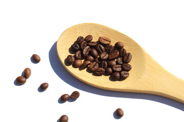 On a white background lies a wooden spoon with coffee beans.