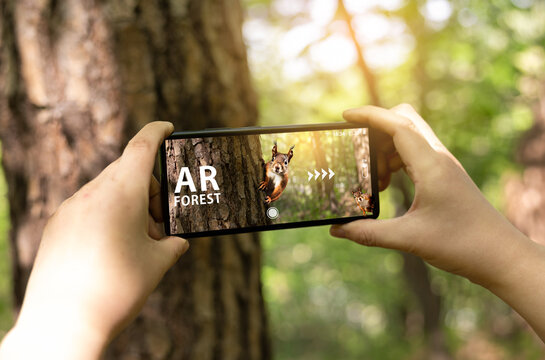 Hand of a woman experiencing an augmented reality (AR) application using a smartphone in the forest