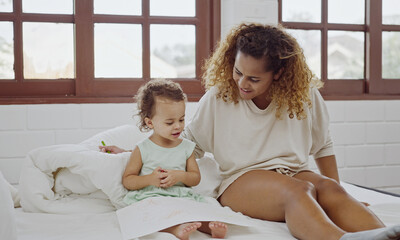 Young mother sitting on bed and drawing with her baby daughter.