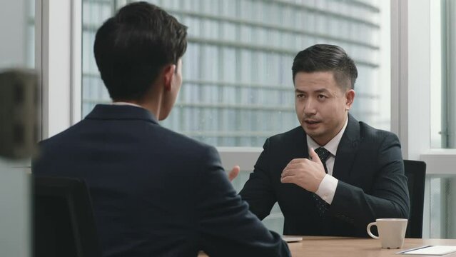 two asian business men sitting at desk having a discussion