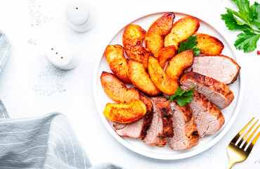 Baked pork tenderloin and quince or apple slices with parsley served on white plate. White table background, top view
