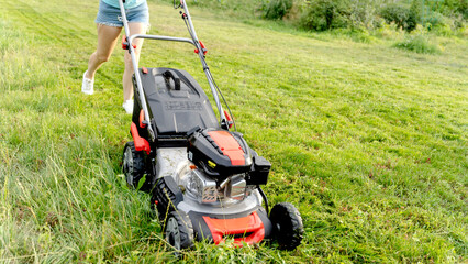 Fototapeta na wymiar a girl with a lawn mower mows a beautiful lawn