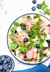 Gourmet salad with sweet pears, blueberries, roquefort cheese, smoked pork ha, arugula and walnuts. White table background, top view
