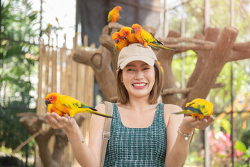 Asian beautiful woman enjoying with bird on hand and body in cage background, Love for animals. Pet...