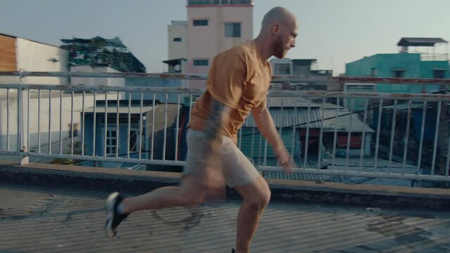 Professional parkour athlete in sportswear running along urban bridge, doing side flip, practicing stunts outdoors in the city. Full length shot