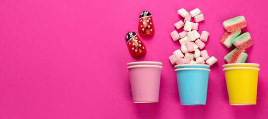 Paper cups with different candies on pink background.