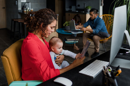 young latin mother working at home using computer while she breastfeeds her baby son in Mexico Latin America, home office concept, hispanic family