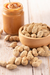 Peanut butter in jar with peanut in wooden bowl on table.