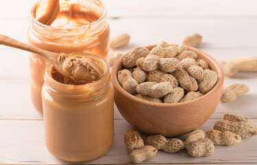 Jar of peanut butter with peanut in wooden bowl on wooden table.