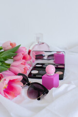 Pink tulips, eye shadow palette with mirror, sunglasses and perfume bottle on white background, women cosmetics set
