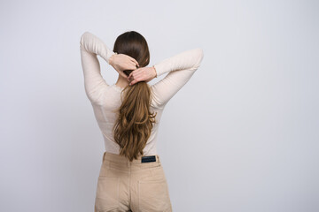Young woman with strong healthy long hair, making a ponytail on white background, back view - obrazy, fototapety, plakaty