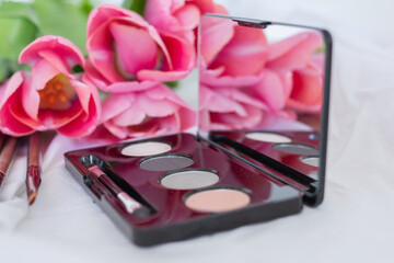 Pink tulips, eye shadow palette with mirror, brushes on white background, women makeup cosmetics set