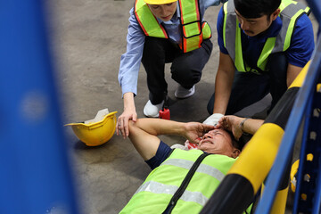 Safety colleagues team helping middle aged warehouse asian worker who had broken head accident and lying on the floor in warehouse while using walkie talkie radio. First aid training concept.