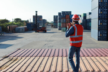 Foreman using tablet and walkie talkie radio control loading containers box. Engineer or worker with safety hat work at container cargo site and checking industrial container cargo freight ship.