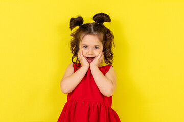 Cute little surprised happy girl in a red dress stands on a yellow background. card, banner. lifestyle. space for text. High quality photo