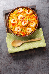 Flavorful Spanish yellow rice and shrimp with vegetables and spices closeup on the plate on the table. Vertical top view from above