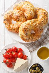 Traditional Turkish acma bread buns with olive oil, olives, cheese, tomato on the table. Vertical top view from above