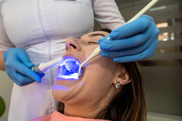  Woman patient receive procedure for teeth whitening bleaching with uv lamp