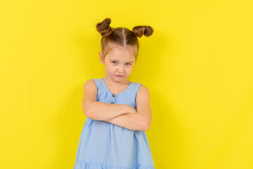 Offended girl crying on a yellow background. a child in a beautiful blue dress pouted her lower lip. Yellow background.