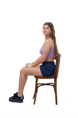 side view of a young girl sitting on chair looking at camera on white background