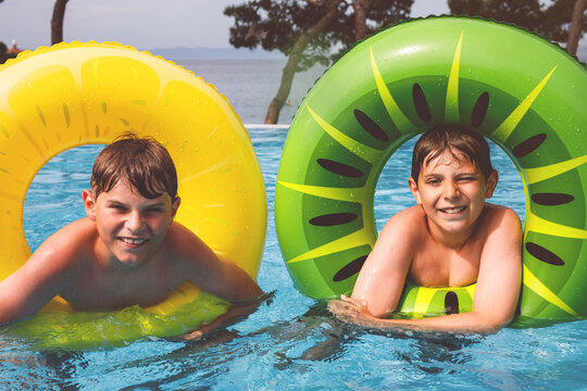 Two kids boys having fun on inflatable rubber rings in outdoor pool. Summer holiday. Summertime kids weekend. Children having fun, brothers on family vacations.