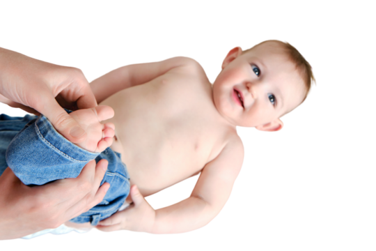 A mother woman puts on jeans pants for a baby boy, isolated on a white background. Mom dresses a happy child in clothes. Kid nine months old