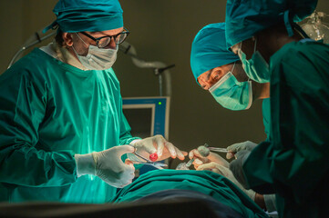 Team of surgery doctor in Operating Room, Assistant Hands out Instruments to Surgeons During Operation. doctor and nurse surgeons in green gown coat at hospital operating theater.