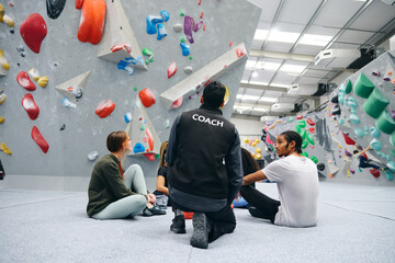 Group Of Friends Being Safety Given Briefing By Male Coach At Indoor Wall Climbing Centre