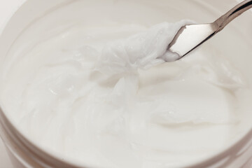 Fototapeta na wymiar White Face Moisturizing Cream in a Cosmetics Jar taken Sample with Spatula, close-up