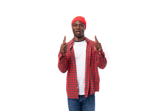 handsome joyful dark-skinned man in a casual plaid shirt points a finger at an advertisement on a white background with copy space