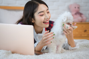 Beautiful asian woman's laptop rang signaling the start of the work meeting but she ignored it for a moment longer to enjoy the playful moment with her dog.