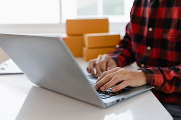 Asian freelance male SME small business entrepreneur working from home Use smartphones and laptops for commercial inspections. online marketing Packaging boxes, SME sellers, concepts, e-commerce teams