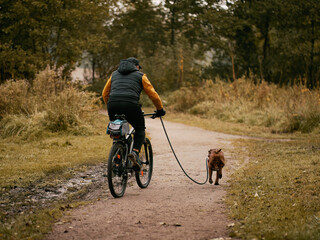 Man rides a bike in the park with his dog
