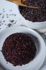 black rice and cooked black rice. This rice has health benefits, is highly nutritious, high in fiber, and has a low glycemic index. suitable for diet. oryza sativa. served on white ceramic plate. 