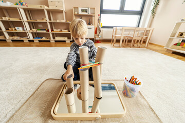 A focused little boy is playing games with Montessori educational toy in kindergarten and building a tower.