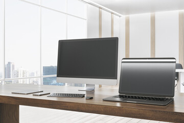 Modern designer office desktop with empty mock up computer screens, supplies and blurry interior with windows and city view background. 3D Rendering.