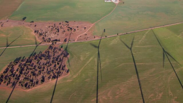 Aerial view of wind turbines spinning in a row with large shadows over an agricultural field in a wind farm producing electricity sustainable energy at sunset, Renewable Energy, Wind Energy, Spain
