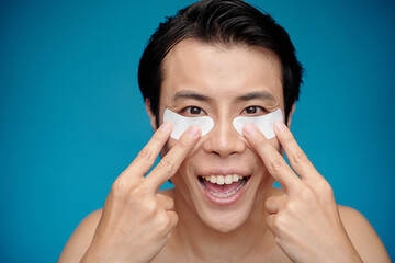 Excited man applying brightening undereye patches when getting ready
