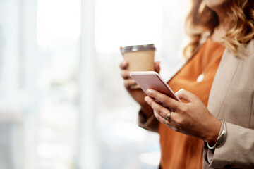 Sending a few messages at the office. an unrecognizable businesswoman drinking coffee and using a cellphone in her office.