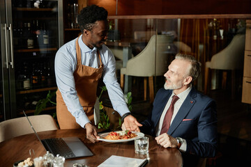 African American waiter serving meal to businessman during lunchtime in restaurant