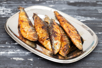 Grilled sardines in metal dish on dark