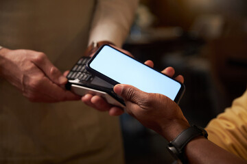 Close-up of customer using smartphone to pay online while waiter holding terminal