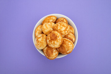 Heap of mini cereal pancakes in bowl on bright background.