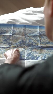 Vertical shot of hand pointing at slopes on ski and hiking map on winter holiday