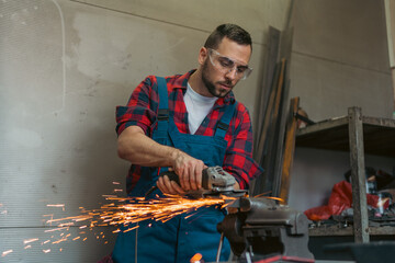 Heavy Industry Engineering Factory Interior with Industrial Worker Using Angle Grinder and Cutting a Metal. Contractor in Safety Uniform and protective glasses cutting metal.