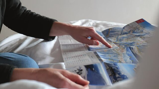 Hands pointing at slopes on ski and hiking map on winter holiday in hotel room