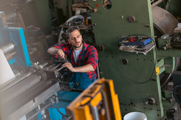 The young craftsman works on a large printing machine in the company.