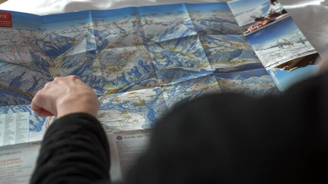 Hand pointing at slopes on ski and hiking map on winter holiday